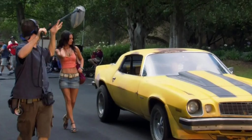 актриса Меган Фокс идет рядом с желтой машиной трансформеров